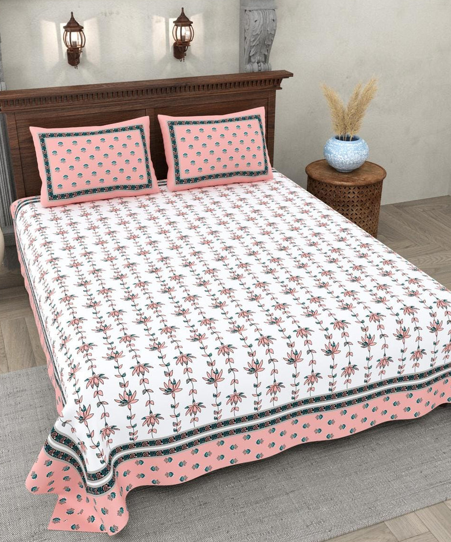 Bed with pink and white floral bedspread and pillows in a bedroom setting.